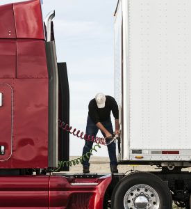 View of a driver connectiing the power cables to trailer of a commercial truck.